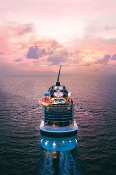 a large cruise ship in the middle of the ocean at sunset with its lights on