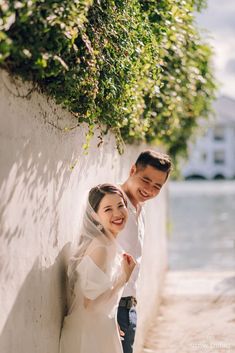 a man and woman standing next to each other near a wall with greenery on it