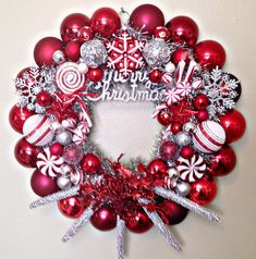 a christmas wreath is hanging on the wall with red ornaments and silver decorations around it