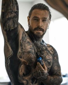 a man with tattoos on his chest holding a bottle in one hand and looking at the camera