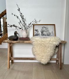 a duck sitting on top of a wooden bench next to a vase