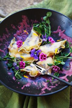 a black plate topped with ravioli and purple flowers