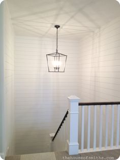 a light fixture hanging from the ceiling in a room with white painted walls and stairs