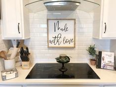 a kitchen with white cabinets and a black stove top in front of a sign that says made with love