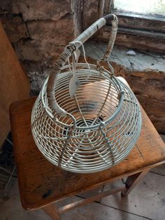 an old metal basket sitting on top of a wooden table next to a brick wall