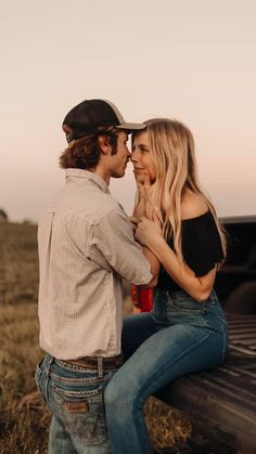 a young man and woman sitting on the back of a pickup truck in an open field