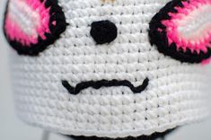 a white crocheted bag with pink eyes and nose on it's head