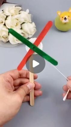 two hands holding toothpicks with fake flowers on the table in front of them