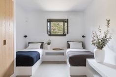 there are two beds in this room with white walls and flooring, along with a window