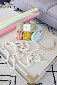 yarn, crochet hooks, and knitting needles on a white tray in front of a couch