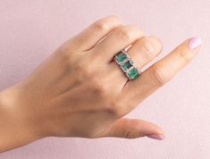 a woman's hand wearing a ring with emeralds and white diamonds on it