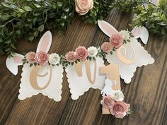 a wooden sign with flowers and bunny ears hanging from it's sides on a table