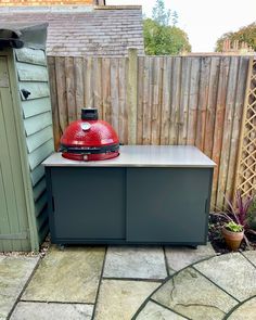 a large red grill sitting on top of a stone patio next to a wooden fence