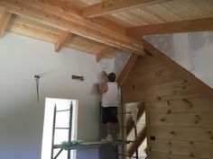 a man standing on a ladder painting the ceiling in a room with wood paneling