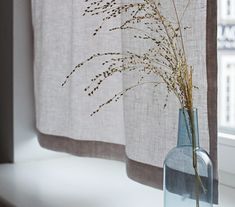 a vase with some dry grass in it next to a window sill and curtain