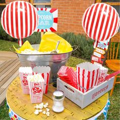 popcorn buckets with red and white striped bags sitting on top of a wooden table