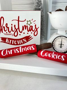 a christmas sign and some cookies are on a counter next to a kitchen scale with a thermometer in front of it