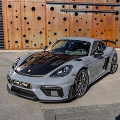 a grey sports car parked in front of a wooden wall