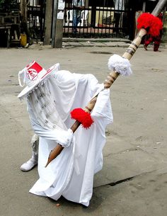 a man dressed in white and holding a stick with red pom poms on it