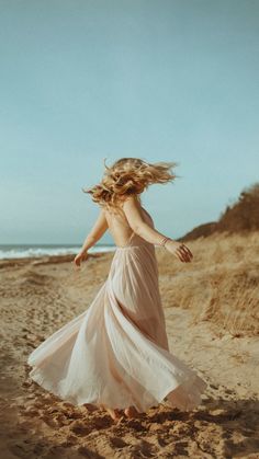 a woman in a long dress running on the beach with her hair blowing in the wind