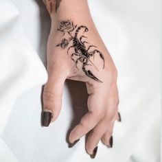 a woman's hand with a scorpion tattoo on it and flowers around the wrist