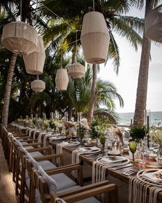 a long table set up with place settings and hanging lanterns over the tables for an outdoor dinner