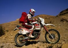 a man riding on the back of a dirt bike down a rocky hill covered in rocks