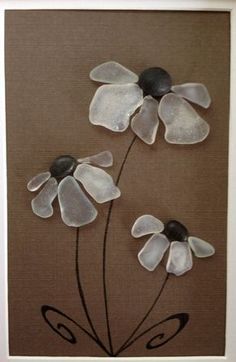 three glass flowers on a brown background in a white frame with black stones and silver accents