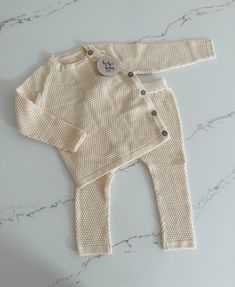 Get ready for cuteness overload with our baby sweater and pants set! Featuring a textured pattern, this long sleeve sweater has buttons on the side for easy dressing. The matching pants have an elastic waistband for a comfortable fit. Perfect for your little one's playful adventures! Beige Long Sleeve Sets With Buttons, Cream Long Sleeve Sets For Fall, Cozy Playtime Sets For Fall, Cozy Long Sleeve Sets For Fall, Fall Long Sleeve Sets With Button Closure, White Knitted Long Sleeve Set, Soft Knit Long Sleeve Sweater For Playtime, Long Sleeve Loungewear Sets With Button Closure, White Long Sleeve Sets With Button Closure