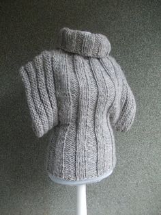 a knitted sweater with a hood is on a white display stand in front of a gray wall