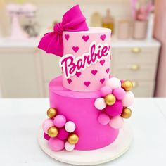 a pink and gold birthday cake with a bow on it's top that says barbie