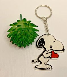 a keychain with a cartoon dog holding a heart next to a green plant