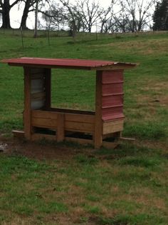 a chicken coop in the middle of a grassy field with trees and grass behind it