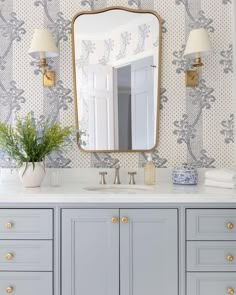 a bathroom with blue and white wallpaper, gold accents and a large mirror over the sink