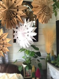 paper snowflakes hanging from the ceiling in a living room with plants and pictures on the wall