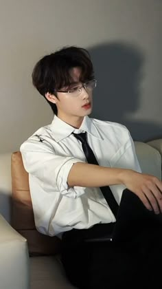 a young man sitting on top of a white couch wearing glasses and a shirt with black tie