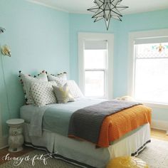 a bed sitting in a bedroom next to two windows and a rug on the floor