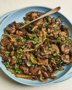 a blue plate topped with mushrooms and parsley next to a wooden spoon on top of a table