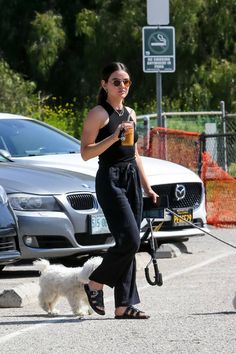 a woman is walking her dog while holding a drink in one hand and an umbrella in the other