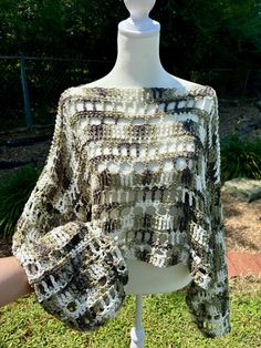 a white mannequin wearing a gray and black crochet sweater on top of grass