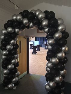 an arch made out of black and silver balloons in the middle of a room with tables