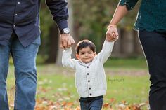 a little boy holding the hands of his parents