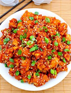 a white plate topped with meat covered in sesame seeds and garnished with green onions