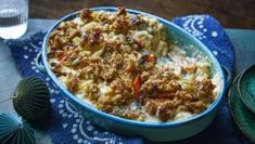 a casserole dish with meat and vegetables in it on a blue towel next to a glass of water