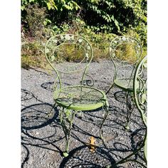 two green metal chairs sitting next to each other on gravel ground with trees in the background