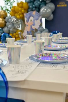 the table is set with blue and white plates, cups, and silver balloons in the background