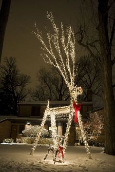 a lighted deer in front of a house with trees and lights on it's back