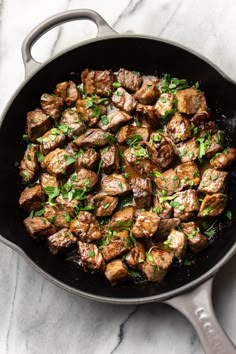 a skillet filled with meat and vegetables on top of a marble countertop next to a spatula