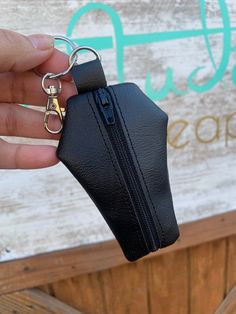 a hand holding a black purse keychain in front of a sign