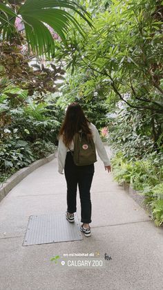 a woman walking down a path in the middle of some trees and plants with her back to the camera